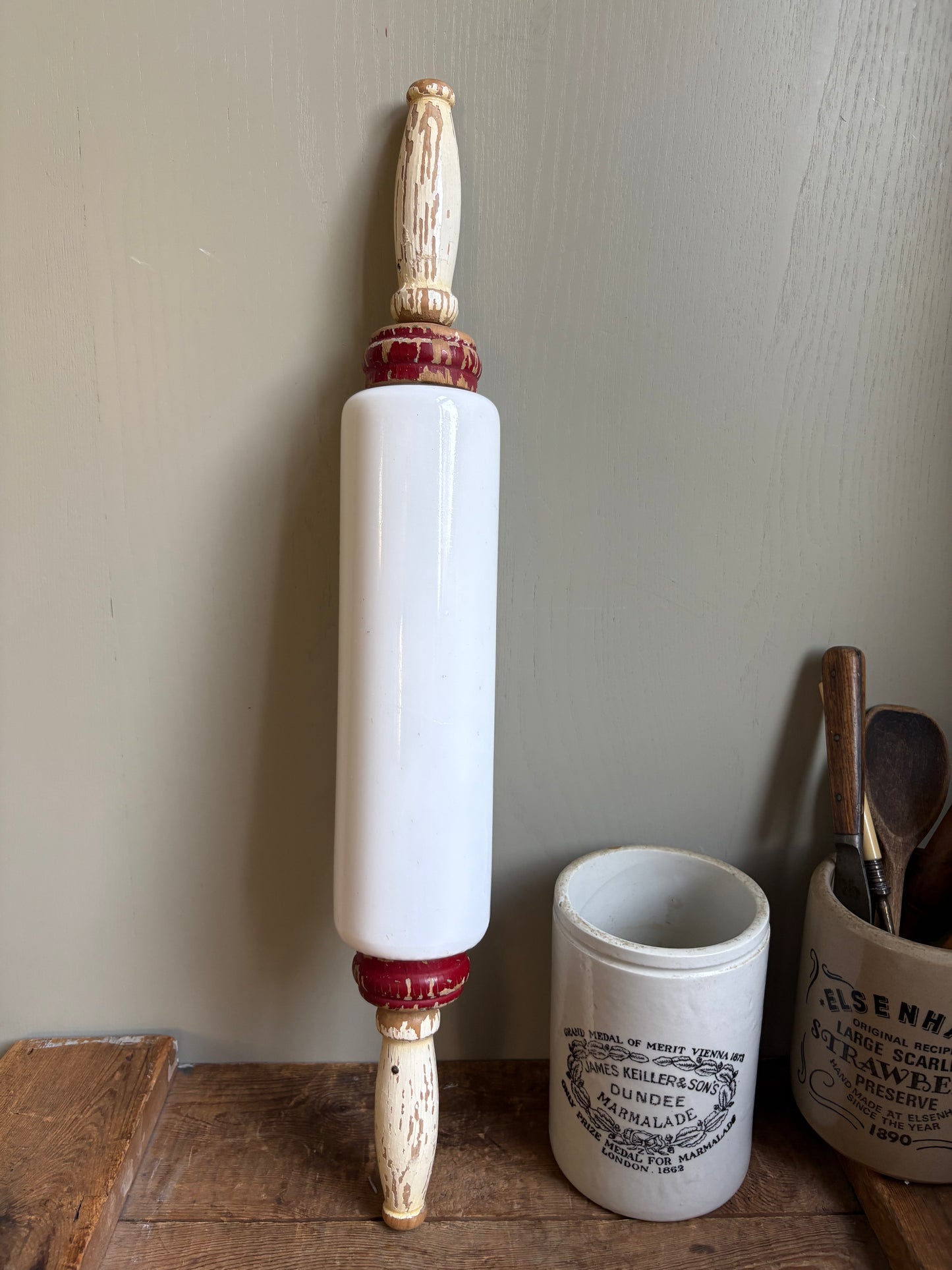A vintage-style wooden rolling pin with a white cylindrical barrel and red decorative accents standing on a wooden surface 